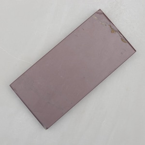 May include: A rectangular sharpening stone with a mauve surface. The stone has a slightly worn appearance with a few small chips on one corner. The stone is designed for sharpening knives and other bladed tools.
