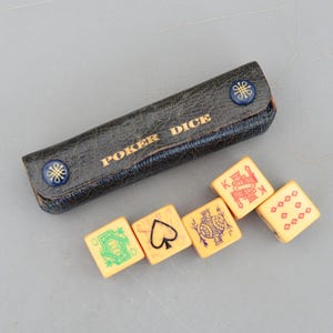 Puede incluir: Un juego de dados de póquer vintage con un estuche de cuero negro. El estuche está grabado con "POKER DICE" en letras doradas y tiene dos botones azules decorativos. Se ven cinco dados de color marfil, cada uno con diferentes símbolos de juego.