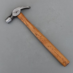 May include: A claw hammer with a wooden handle and a steel head. The hammer head is silver and has a curved claw for removing nails. The handle is made of light brown wood. The hammer is designed for carpentry and construction tasks.