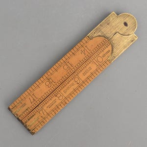 May include: A vintage folding wooden ruler with brass hinges and fittings. The light brown wood features black numerical markings from 7 to 17, with text reading Rabone, No 1380, Made in England, and Warranted Boxwood clearly visible on the surface.