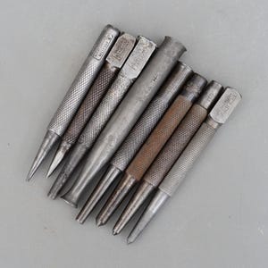 Könnte beinhalten: Ein Satz von acht Lederstanzern aus Metall mit verschiedenen Spitzen. Die Stanzern sind silberfarben und haben einen strukturierten Griff. Die Spitzen sind alle in verschiedenen Formen und Größen. Einige der Stanzern haben Markierungen, darunter die Wörter "EDGE" und "BRITISH MADE".