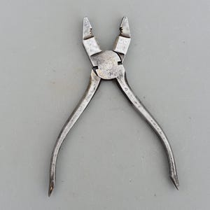 Peut inclure: Une pince à becs courbes de couleur argentée avec une petite inscription sur la poignée indiquant "GERMANY 40".