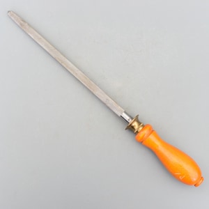 以下が含まれることがあります： オレンジ色の木製のハンドルが付いた、長い銀色の鋼製のナイフシャープナー。ハンドルの上部に真鍮のリングが付いています。