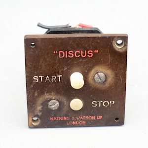 May include: A brown metal panel with two white buttons labelled "Start" and "Stop". The panel also has the text "DISCUSS" and "WATKINS & WATSON LTD LONDON" in red lettering.