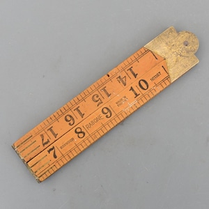 Peut inclure: Une règle pliante orange avec des marquages noirs et un raccord en laiton. La règle est marquée de chiffres de 17,78 cm à 43,18 cm. Le texte "RABONE" et "BOXWOOD" sont visibles. La règle est fabriquée en Angleterre.
