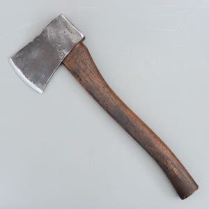 May include: A vintage axe with a dark wooden handle and a steel head. The axe head has a slightly curved blade and the word "HERCULES" is stamped on the metal. The handle is a dark brown colour.