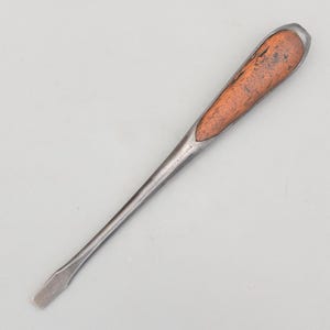 May include: A flathead screwdriver featuring a dark, weathered metal shaft and a distinct wooden handle insert. The metal shank is tapered and shows signs of age, with the word SHEFFIELD clearly stamped into the side of the metal near the handle.