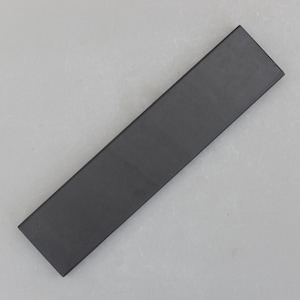 May include: A rectangular, dark gray object with a matte finish. The object is long and narrow, with a flat top and sides. The item is positioned diagonally against a light gray background.