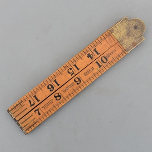 Peut inclure: Une règle pliante en bois de couleur marron clair avec des chiffres noirs et des marquages. Elle mesure jusqu'à 43 cm. On peut lire les inscriptions « RABONE » et « MADE IN ENGLAND ». Les charnières sont en laiton.