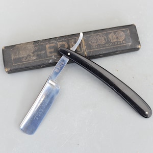 以下が含まれることがあります： 黒いハンドルと銀色の刃を持つストレートシェーバー。刃には「ERN」と「TRYX SOLINGEN」の刻印があります。シェーバーは、「ERN」と「WALD-SOLINGEN」の文字が書かれた黒いケースに入っています。