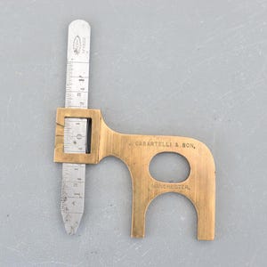 May include: A brass tool with a ruler and a ring gauge. The tool is marked "J. Casartelli & Son, Manchester".