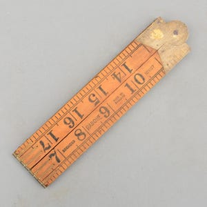 May include: A vintage wooden folding ruler, featuring measurements in inches. The ruler is made of boxwood and has brass hinges. The numbers are printed in black ink. The ruler is marked "Made in England".