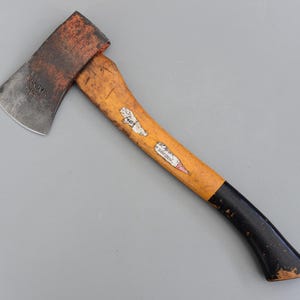 Könnte beinhalten: Eine Vintage-Axt mit Holzgriff und Metallkopf. Der Axtkopf ist mit "SANDVIK SWEDEN" markiert. Der Griff ist gelb lackiert mit Schwarz am Ende. Die Axt weist Gebrauchsspuren auf.