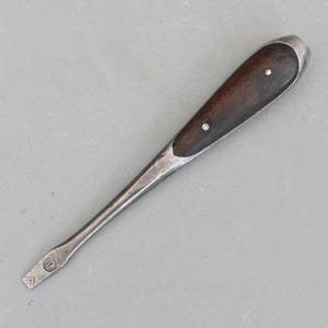 May include: A vintage flathead screwdriver with a dark wooden handle and a metal shaft. The handle is secured with two small rivets. The tip of the screwdriver has a flat blade and a stamped number 9.