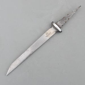 May include: A silver-coloured dagger with a long, pointed blade. The handle has a circular guard and a textured grip. The blade has the text "W. M. HORSFALL & SONS SHEFFIELD".