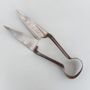 May include: Antique silver shears with a curved handle and pointed blades. The shears are marked "The Ideal Shears, Made in England".