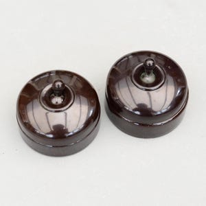 May include: Two vintage, dark brown, round light switches with a toggle lever. The switches have a glossy finish and are set against a light background. These classic switches are a great addition to any home.