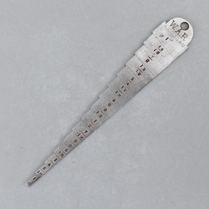 May include: A vintage metal gauge with a series of stepped measurements. The gauge is marked with fractions and the text "W.A.R. A. COGGAN". The tool is designed for measuring small increments, likely in inches.