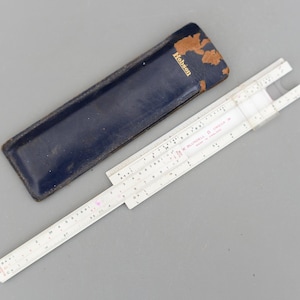 Peut inclure: Une règle à calcul vintage avec un corps blanc et des marquages noirs, à côté d'un étui en cuir bleu foncé. L'étui porte le nom "Hobson". C'est un instrument mathématique pour les calculs.