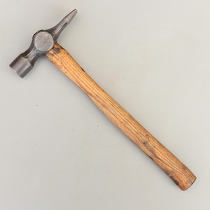 May include: A metal hammer with a wooden handle. The hammerhead has a round striking face on one side and a pointed peen on the other. The handle is made of light brown wood.