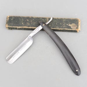 May include: A vintage straight razor with a black handle and a silver blade. The blade is inscribed with "JOHN CLARK & SON, SHEFFIELD, ENGLAND" and "HOLLOW GROUND".