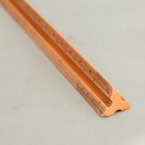 May include: A vintage wooden triangular ruler with etched markings. The ruler is a warm, light brown colour and features measurements along its edges. The ruler is designed for drafting and technical drawing.