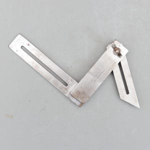 May include: A metal adjustable square tool with a slotted arm and a pivoting blade. The tool is made of silver-coloured metal and has the text "MADE IN FINLAND" and "PAT.4743" stamped on it. The tool is designed for measuring angles.