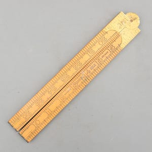 Könnte beinhalten: Ein alter, zusammenklappbarer Holz-Zollstock mit Zentimeter-Messungen von 25 bis 66. Der Zollstock ist aus hellem Holz mit schwarzen Markierungen und Text, einschließlich "Made in England" und der Marke "Rabone".