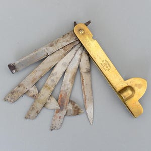 以下が含まれることがあります： 真鍮製のハンドルと複数の鋼鉄製の刃が付いた、アンティークのマルチブレードナイフ。 刃は扇状に広げられており、摩耗や経年劣化の兆候が見られます。 真鍮製のハンドルには「QUALITY B G SUPERIEURE」の文字が刻まれています。