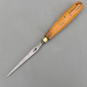 May include: A vintage awl with a wooden handle and a metal blade. The handle is light brown with dark streaks and a brass ferrule. The blade is silver and tapers to a point. The text "TYZACK SHEFFIELD" is visible on the blade.