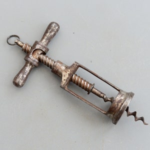 Può includere: Un cavatappi in metallo vintage con un manico a forma di T e un cavatappi a spirale. Il cavatappi è arrugginito e ha una finitura usurata.