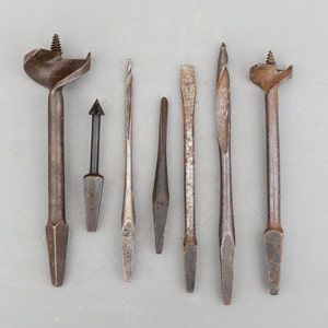 May include: A set of eight vintage wood drill bits, including a twist drill bit, a spade bit, and a countersink bit. The drill bits are made of metal and have a variety of sizes and shapes.