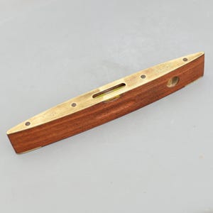 May include: A vintage wooden level with brass accents. The level has a rectangular shape with a dark wood body and brass end caps and trim. A small bubble level is visible in the center. The tool is designed for measuring horizontal and vertical alignment.