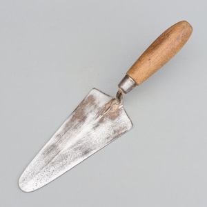 May include: A vintage trowel with a wooden handle and a metal blade. The blade is worn and has a patina from use.