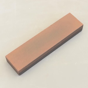 Peut inclure: Une pierre à aiguiser rectangulaire avec une couche supérieure brune et une couche inférieure noire. La pierre est utilisée pour aiguiser les couteaux.