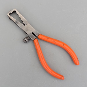 May include: A wire stripper tool with a metal body and bright orange handles. The tool has a curved design with a cutting edge and an adjustable screw. The handles are made of a smooth, non-slip material.
