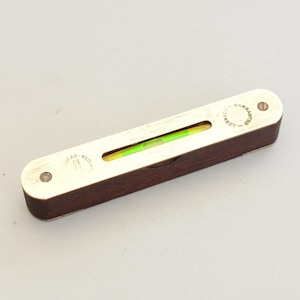 Peut inclure: Un niveau à bulle vintage avec un corps en bois foncé et des détails en laiton. Le niveau comporte un tube en verre transparent avec une bulle verte. Le laiton est gravé des mots "Warranted Correct" et "Lucas & Victa".