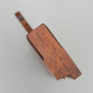 May include: A vintage wooden tool, featuring a rectangular body and a slender handle. The tool is a warm brown hue, showcasing the wood grain. The text "G. GOWER H. R. M. & SON Sims London" is etched on the surface.