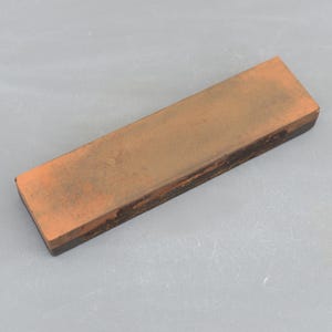May include: A rectangular brown sharpening stone with a black rubber base.
