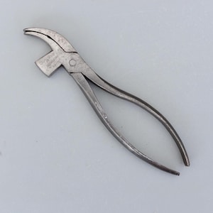 Puede incluir: Una herramienta metálica vintage con una cabeza curva y mangos largos. La herramienta tiene una función similar a un martillo en la cabeza y probablemente se utiliza para una tarea específica. El metal tiene un aspecto desgastado y envejecido.