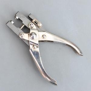 Może przedstawiać: Biały ceramiczny kubek z czarnym uchwytem i napisem "But First, Coffee" czarną, pogrubioną czcionką. Kubek stoi na białej powierzchni.