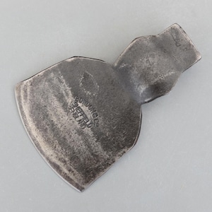 Op de afbeelding: Een stalen bijlkop met een gebogen blad en een platte bovenkant. De tekst "BOWDON & CO SHEFFIELD ENGLAND" is op de bijlkop gestempeld. De bijlkop is donkergrijs van kleur.