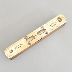 May include: A vintage spirit level, featuring a wooden body and brass detailing. The brass plate is marked with "Warranted Correct" and "J. MARSHALLWOOD 1910". It has two bubble vials for precise measurements.