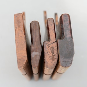 Puede incluir: Una colección de cuatro cepillos de moldura de madera antiguos, cada uno con un perfil diferente. Los cepillos están hechos de madera oscura y muestran signos de edad y uso. Algunos cepillos tienen texto tallado en la madera, incluyendo los nombres "H. WALKER" y "J. AWCKERKE A. CLARKE".