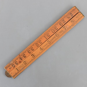 以下が含まれることがあります： 35インチ（88.9 cm）まで測定できる、木製の折りたたみ定規。明るい色の木材に黒い目盛りと数字が記されています。「RABONE」と「MADE IN ENGLAND」の文字が見えます。定規は部分的に開いており、折りたたみ式のデザインを示しています。