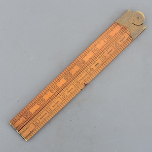 Puede incluir: Una regla plegable de madera vintage con accesorios de latón. La regla está marcada con medidas en pulgadas y números. La madera es de color marrón claro y el latón tiene un aspecto deslustrado. La regla está etiquetada como "Boxwood" y "Made in England".