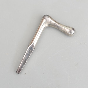 Peut inclure: Un outil en métal argenté avec une poignée coudée et une extrémité pointue. L'outil porte le numéro "2" gravé près de l'extrémité pointue. La poignée est arrondie et légèrement texturée.