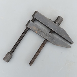 Könnte beinhalten: Ein Vintage-Werkzeug Eclipse Nr. 412, wahrscheinlich eine Klemme oder ein Schraubstock, aus dunklem Metall. Das Werkzeug hat zwei parallele Backen, die durch Gewindestangen und einen Anziehmechanismus verbunden sind. Der Text "ECLIPSE No. 412 Made in England" ist sichtbar.