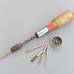 Puede incluir: Un juego de destornilladores vintage con mango de madera y broca de metal. El juego incluye cinco puntas de destornillador de diferentes tamaños.