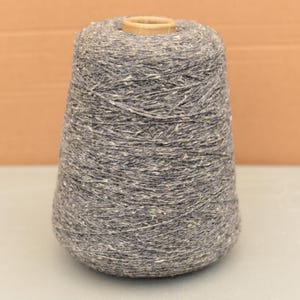 Peut inclure: Un grand cône de fil gris avec des mouchetures blanches et beiges. Le fil est étroitement enroulé autour d'un noyau en carton. Le cône a une forme conique, plus large à la base et se rétrécissant vers le haut.